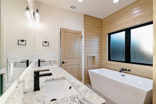 bathroom featuring wood walls, a sink, visible vents, a freestanding bath, and double vanity