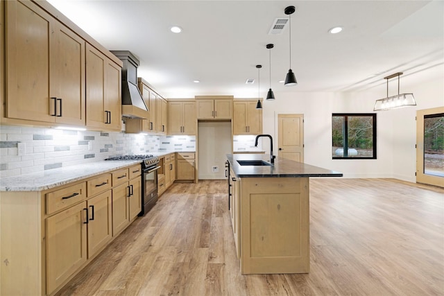 kitchen featuring pendant lighting, a center island with sink, custom exhaust hood, black gas range oven, and a sink