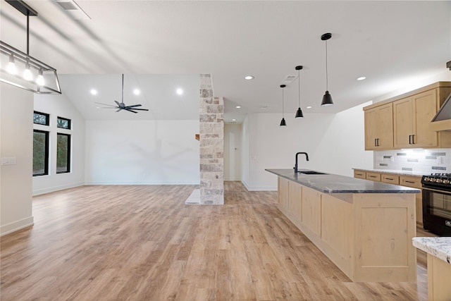 kitchen featuring light brown cabinets, a sink, black gas stove, hanging light fixtures, and a center island with sink