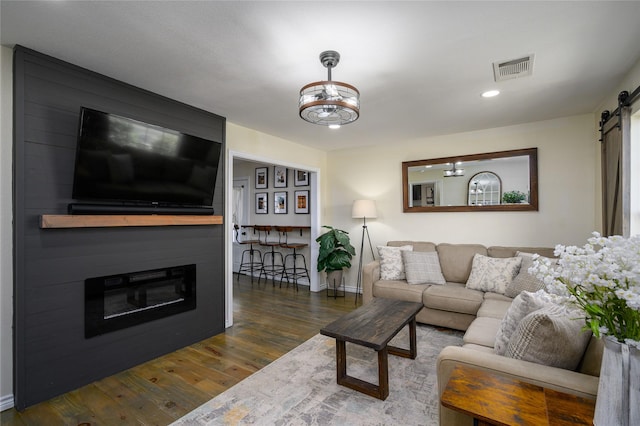 living room with a barn door, visible vents, dark wood finished floors, baseboards, and a glass covered fireplace