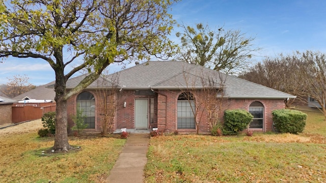 view of front of property featuring brick siding, roof with shingles, fence, and a front yard