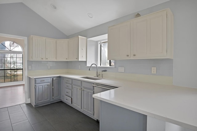 kitchen with dishwasher, backsplash, vaulted ceiling, light countertops, and a sink