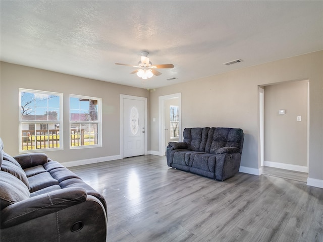 living area featuring visible vents, a textured ceiling, baseboards, and wood finished floors