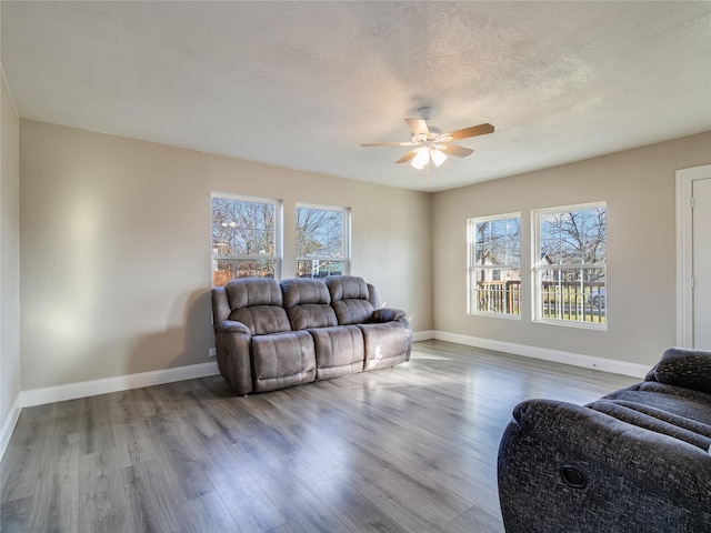 living area featuring a textured ceiling, ceiling fan, wood finished floors, and baseboards