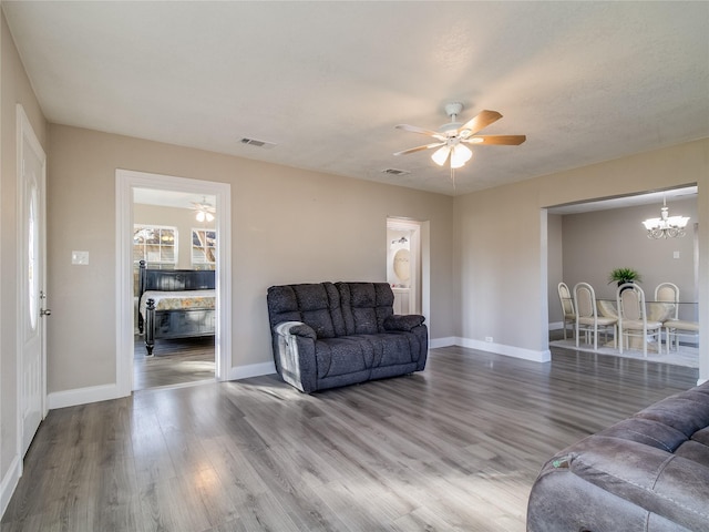 living area with ceiling fan with notable chandelier, wood finished floors, visible vents, and baseboards