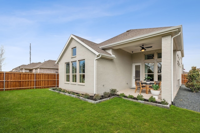 rear view of house featuring ceiling fan, brick siding, a lawn, and a fenced backyard