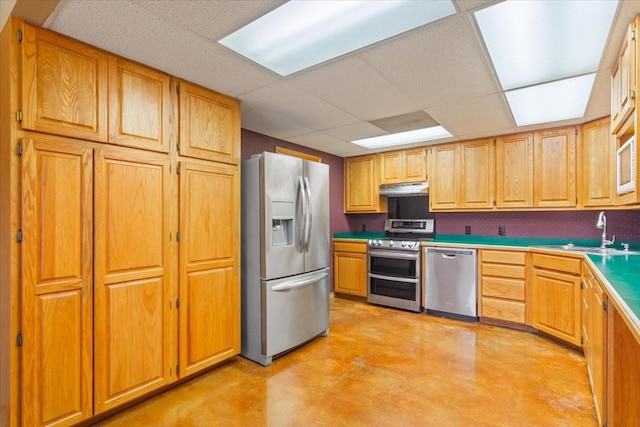 kitchen featuring appliances with stainless steel finishes, light countertops, concrete flooring, under cabinet range hood, and a sink