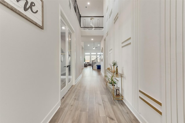 hallway with light wood-style floors, french doors, a towering ceiling, and baseboards