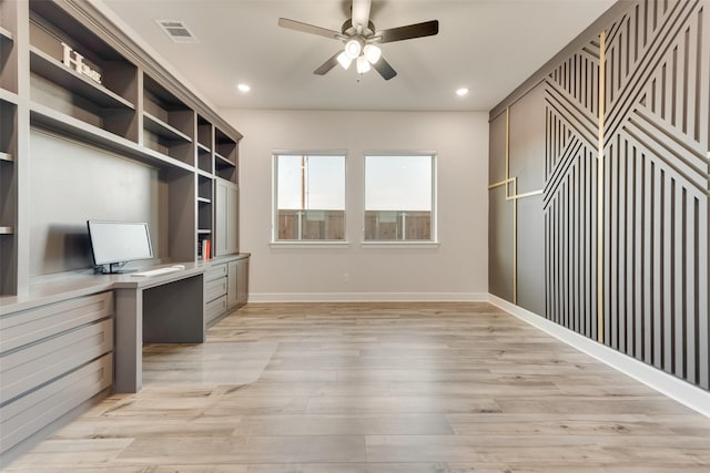 office featuring built in desk, light wood-type flooring, visible vents, and a ceiling fan