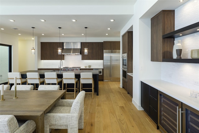 kitchen with wall chimney exhaust hood, modern cabinets, appliances with stainless steel finishes, decorative light fixtures, and light countertops