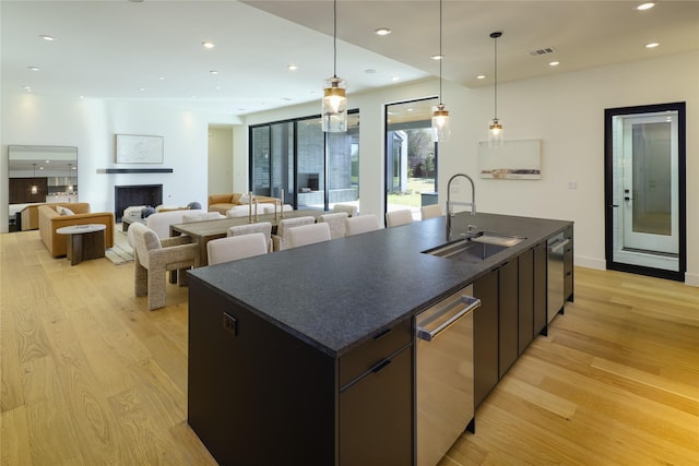 kitchen with open floor plan, an island with sink, dark countertops, and a sink