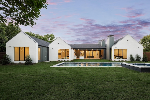 rear view of house featuring a pool with connected hot tub, a lawn, and a chimney