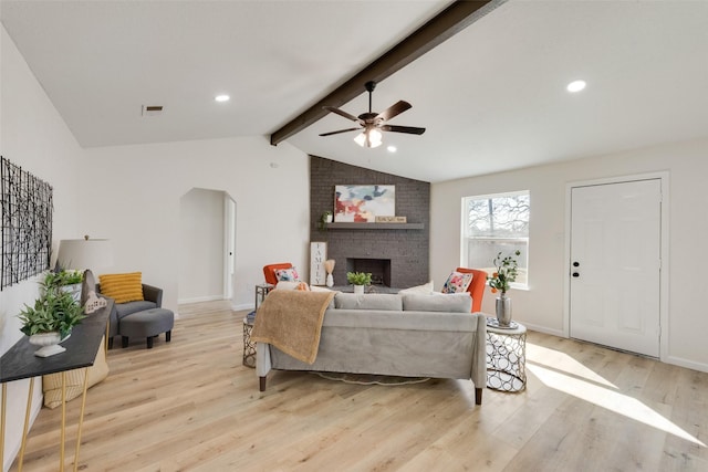 living room with arched walkways, a fireplace, vaulted ceiling with beams, visible vents, and light wood-style flooring