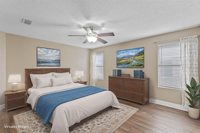 bedroom with a textured ceiling, light wood finished floors, multiple windows, and visible vents