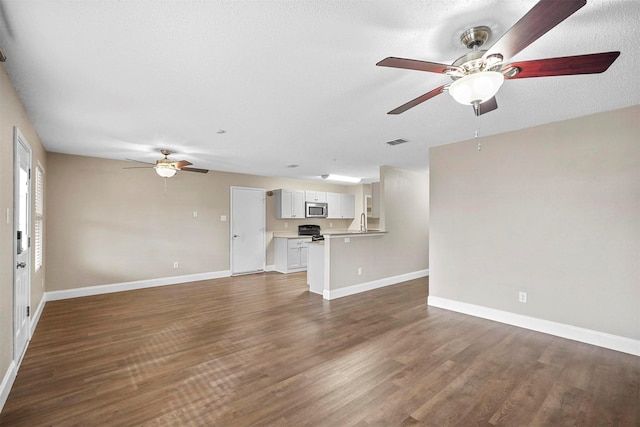 unfurnished living room featuring dark wood-style flooring, a sink, a ceiling fan, visible vents, and baseboards