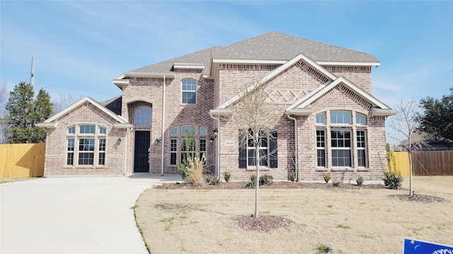 french country inspired facade featuring a shingled roof, brick siding, fence, and a front lawn