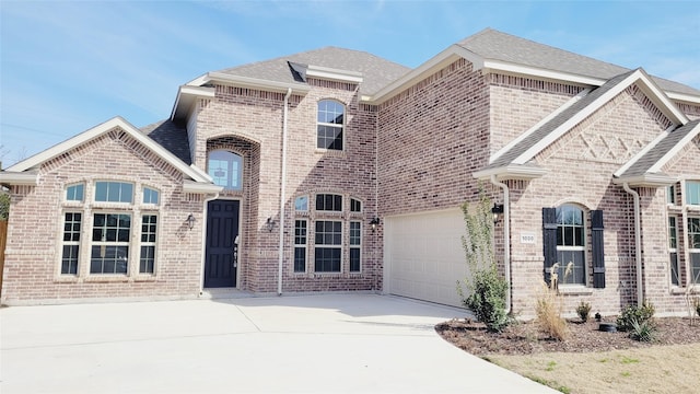 french country home featuring concrete driveway, brick siding, and an attached garage