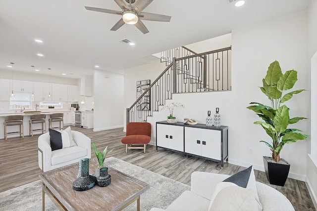 living room featuring light wood finished floors, baseboards, a ceiling fan, stairway, and recessed lighting