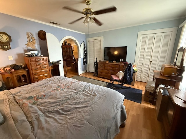 bedroom featuring arched walkways, visible vents, light wood-style floors, ornamental molding, and two closets