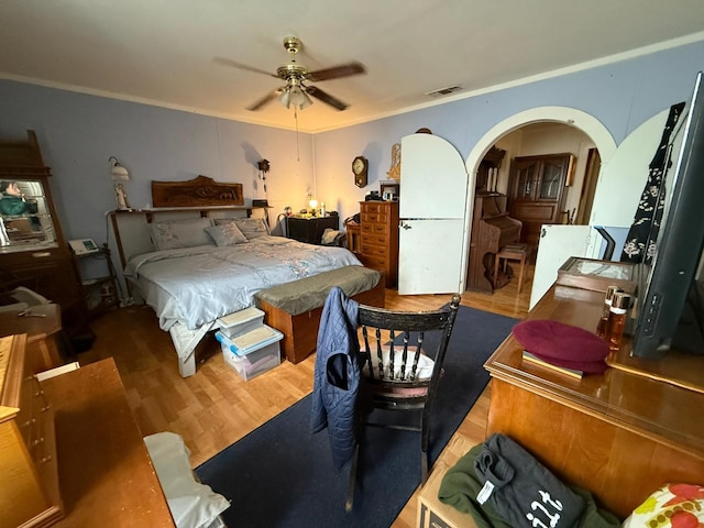 bedroom with visible vents, arched walkways, ceiling fan, wood finished floors, and crown molding