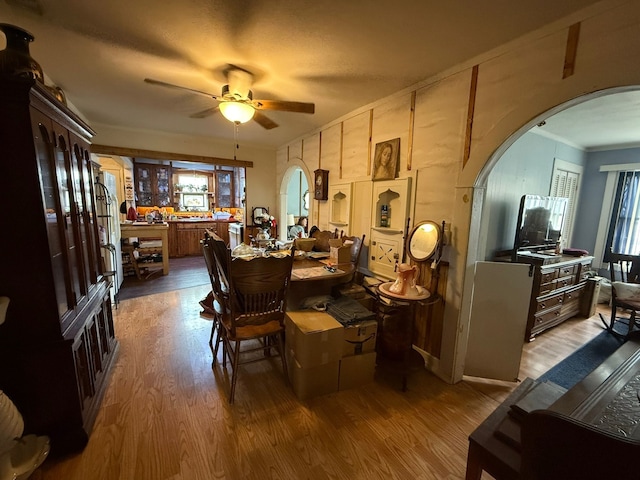 dining space with ceiling fan, crown molding, arched walkways, and wood finished floors