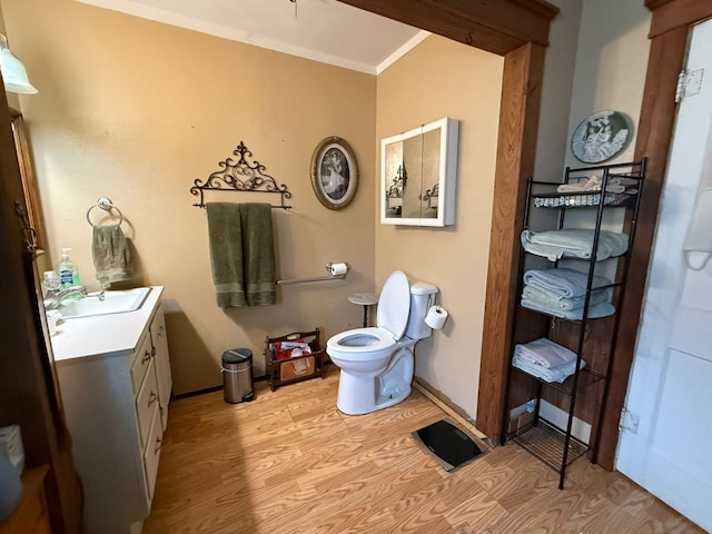 bathroom featuring crown molding, toilet, vanity, wood finished floors, and baseboards