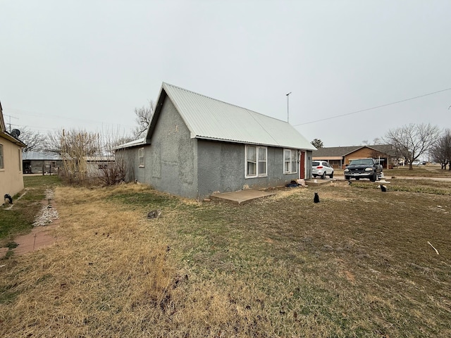 view of side of property with metal roof, a lawn, and stucco siding