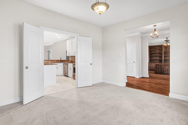 empty room featuring a notable chandelier, light colored carpet, a sink, baseboards, and ornamental molding