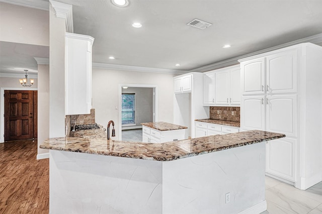 kitchen featuring light stone counters, white cabinets, visible vents, and a peninsula