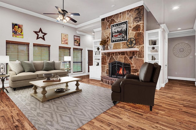 living area featuring baseboards, ceiling fan, wood finished floors, crown molding, and a stone fireplace