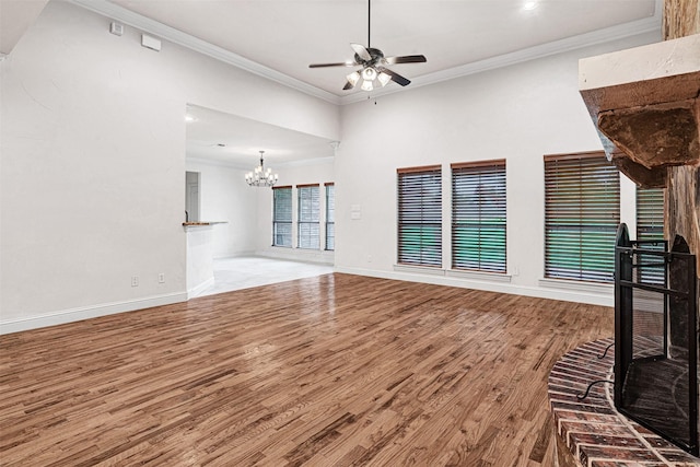 unfurnished living room featuring ceiling fan with notable chandelier, ornamental molding, wood finished floors, and baseboards