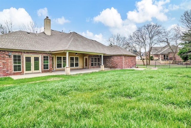 rear view of house featuring a patio, brick siding, a shingled roof, fence, and a lawn