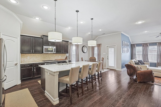 kitchen featuring a sink, a kitchen breakfast bar, open floor plan, appliances with stainless steel finishes, and tasteful backsplash