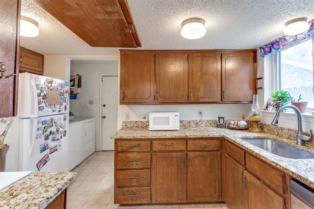 kitchen with brown cabinets, light tile patterned flooring, a sink, white appliances, and independent washer and dryer