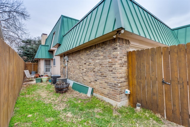 view of property exterior with metal roof, brick siding, fence, a standing seam roof, and a chimney