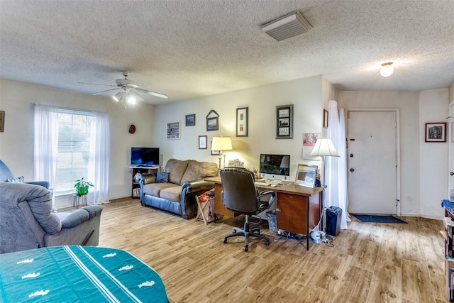 office space with visible vents, ceiling fan, light wood-style flooring, and a textured ceiling