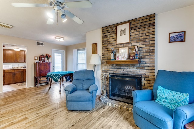 living area featuring visible vents, a fireplace, a textured ceiling, and light wood finished floors