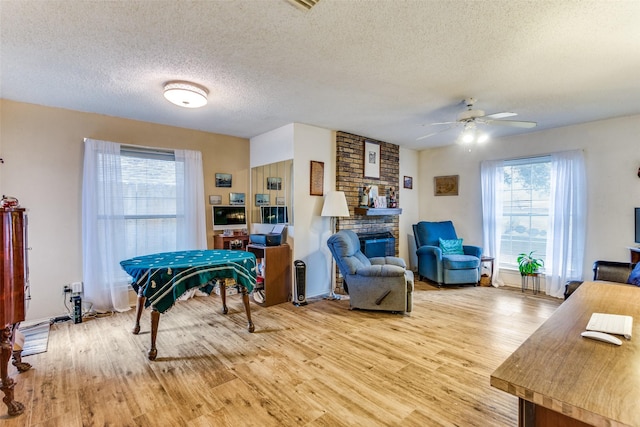 living area with a large fireplace, a textured ceiling, a ceiling fan, and wood finished floors