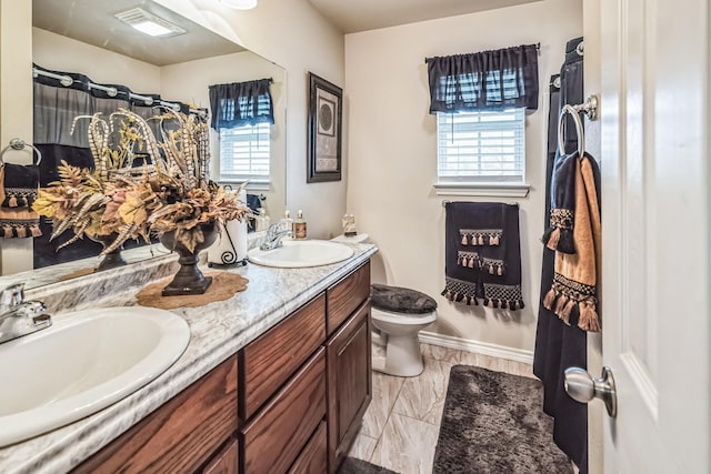 full bath featuring baseboards, a sink, toilet, and double vanity