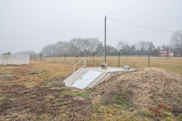 entry to storm shelter with a rural view and fence