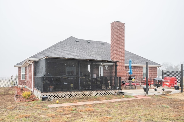 rear view of property with a chimney, a shingled roof, a lawn, a sunroom, and a patio area