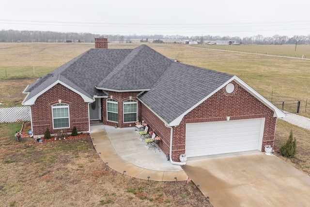 view of front of house featuring driveway, a garage, roof with shingles, a rural view, and brick siding