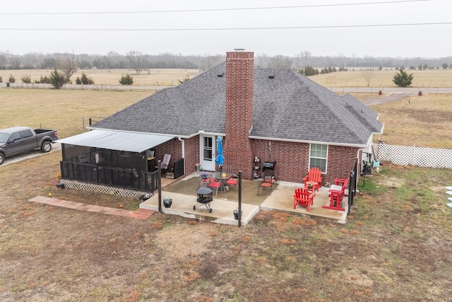 rear view of house with brick siding, a patio, a chimney, roof with shingles, and a sunroom