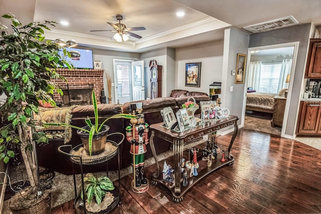 living room with wood finished floors, a ceiling fan, visible vents, a tray ceiling, and crown molding