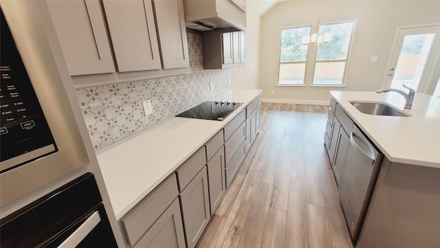 kitchen featuring hanging light fixtures, light countertops, black appliances, premium range hood, and a sink