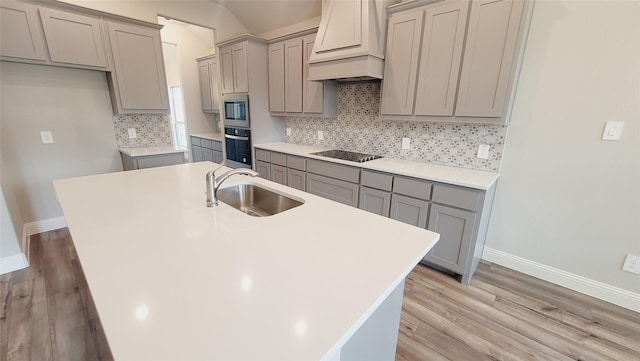 kitchen with light countertops, wall oven, a sink, an island with sink, and premium range hood