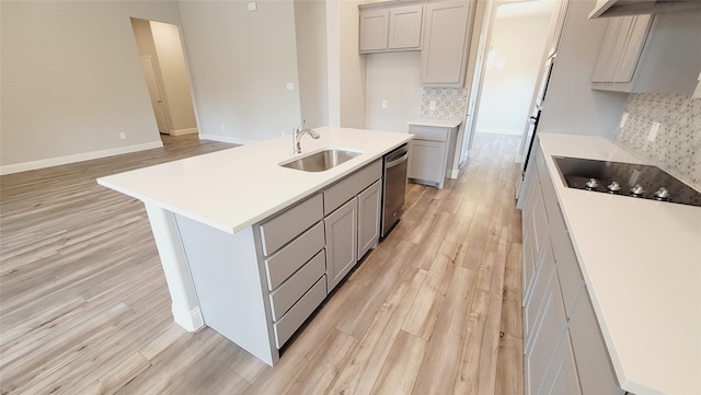 kitchen with dishwasher, a kitchen island with sink, light countertops, gray cabinetry, and a sink