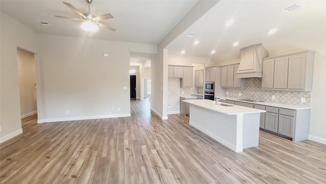 kitchen with custom range hood, appliances with stainless steel finishes, gray cabinets, light countertops, and backsplash