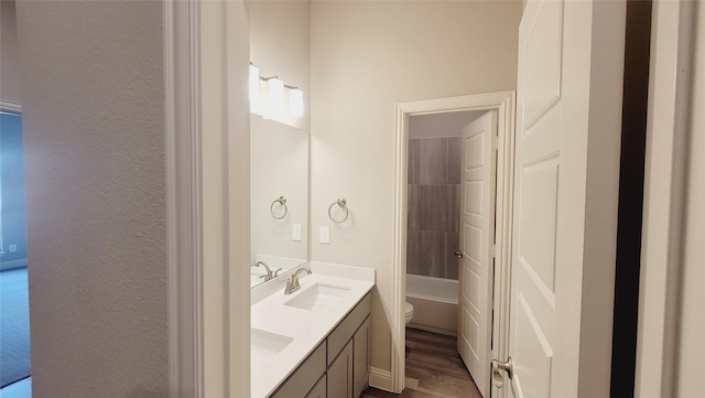 bathroom with double vanity, toilet, a sink, shower / tub combination, and wood finished floors