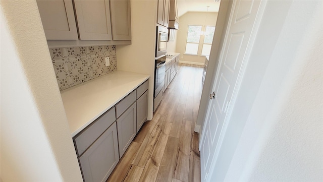 corridor with lofted ceiling, light wood-type flooring, baseboards, and an inviting chandelier